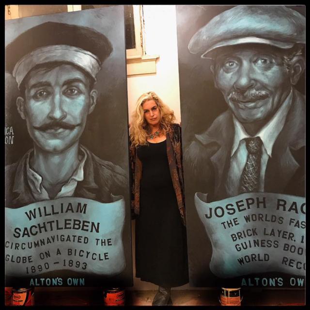 Photo of Mason standing between her two portraits, which have since been hung at the Post Commons. Taken from Mason's Facebook page and used with permission.