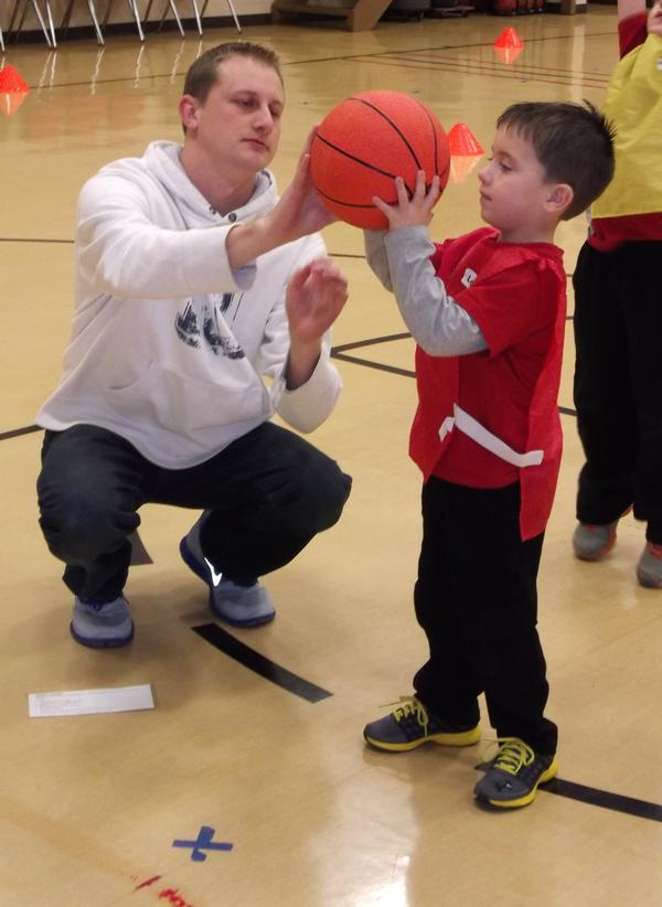 Logan Kuehnel, 5, learns how to properly hold the basketball at the shooting station from the station leader, Steven Goetten.
