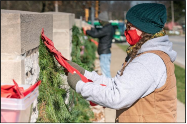 L&C Gardener/Landscaper Katie Piper and L&C Horticulture Manager Ethan Braasch (background) hang evergreen holiday décor along the campus wall on Godfrey Road Tuesday, Dec. 1. The Godfrey Women's Club donated money to purchase the decorations. The display provides a warming scene to those passing by. Photo by Nathan Woodside, L&C Media Services