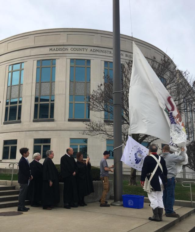 Madison County employees from Facilities Management assist in raising the Bicentennial flag during a ceremony Monday to kickoff the 200th birthday celebration. Chairman Kurt Prenzler, far left, and Judges Philip Alfred and Dennis Ruth, Chief Judge David Hylla and Judge Sarah Smith, along with Madison County Historical Museum Director Jon Parkins watch as the flag go up.