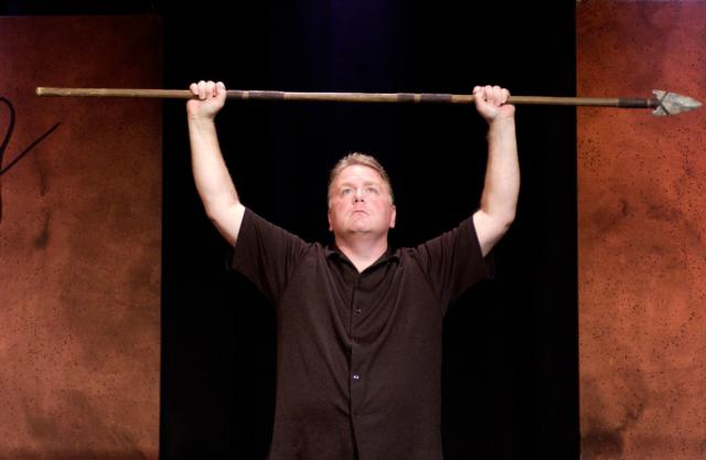 Comedian Kevin Burke with a spear over his head.