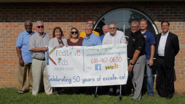 Kreative Kids Learning Center representatives and supporters announce the purchase of their new Godfrey location, pictured in the background, on July 20, 2022. The organization will officially move into this location at the end of March.