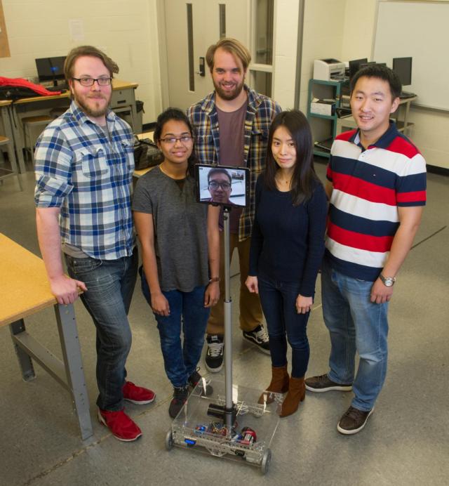 The SIUE School of Engineering research team working on the telepresence robot includes (L-R) Alex Dinan, Sherin John, Bryan Kier, Kai Li and Pengji Duan. Dr. Mingshao Zhang is seen on the robot’s screen via remote access.