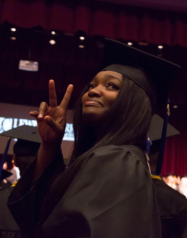 A graduate signals to her guests in the audience during the Commencement ceremony inside the Hatheway Cultural Center’s Ann Whitney Olin Theatre. Photo by Jan Dona, L&C Media Services