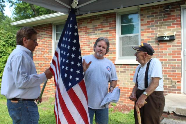 Alton Mayor Brant Walker and Rodney Cook hand World War II veteran Thomas Lowe his American flag.