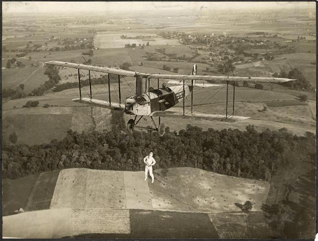 Charles Fower pilots a Standard J-1 biplane as Bertie Brooks dangles from the plane by his teeth as part of a Marie Meyer Flying Circus performance. Missouri Historical Society. Identifier: N30267