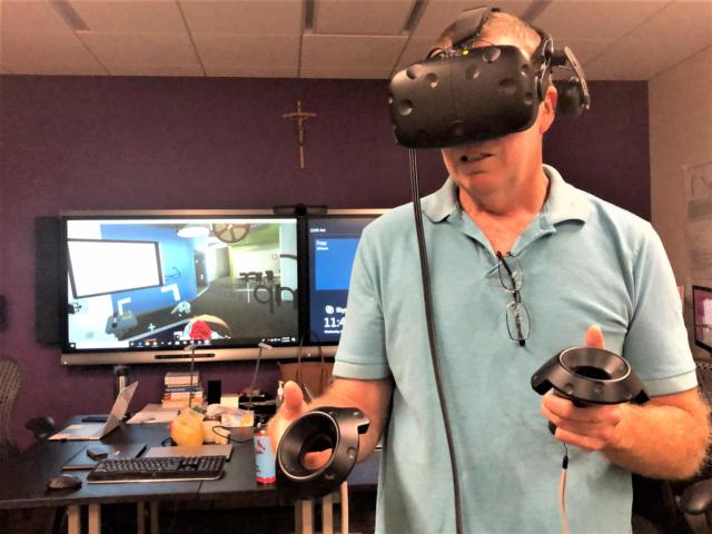 Marquette High School Science Department Chair John Walters dons Virtual Reality headset and controllers to experience the immersive technology used to train and in some cases prepare for complex surgeries.