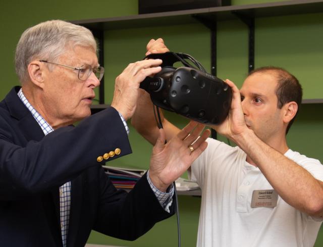 Associate Prof. Edward Ackad helping Senator Bill Haine with virtual reality glasses.