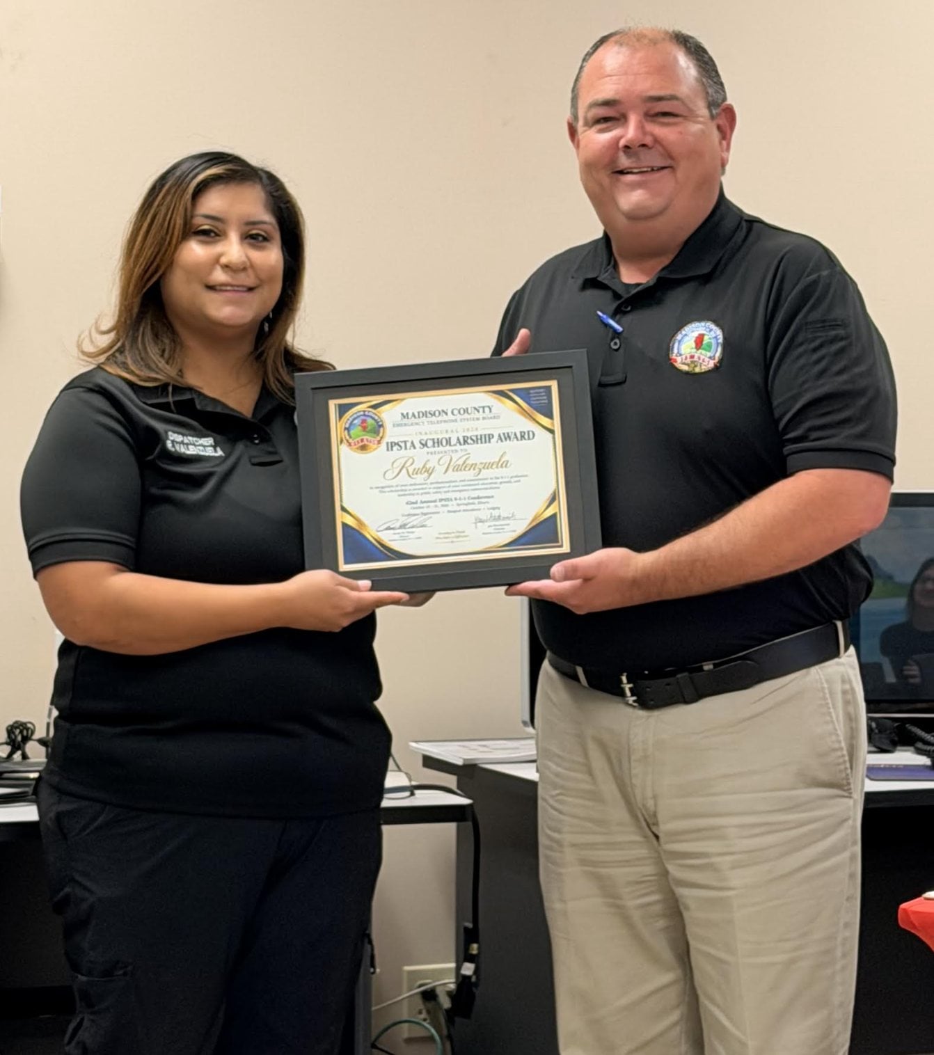 911 Director Arron Weber (right) presents Granite City Telecommunicator Ruby Valenzuela with the inaugural scholarship to attend the statewide 911 Illinois Public Safety Telecommunicators Association conference in October. The conference will cover all expenses for the event.